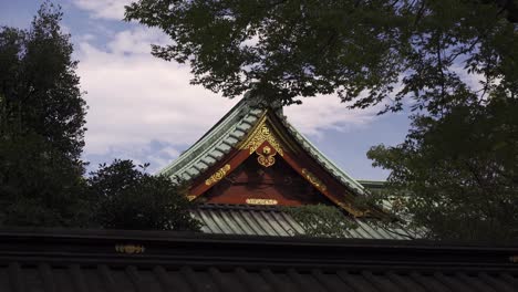 hermoso templo japonés rojo y dorado contra el cielo azul nublado recortado entre árboles - tiro cerrado