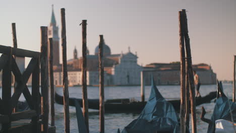 Gondeln-Vertäut-An-Holzpfählen-Mit-Blick-Auf-Die-Kirche-San-Giorgio-Maggiore-In-Venedig