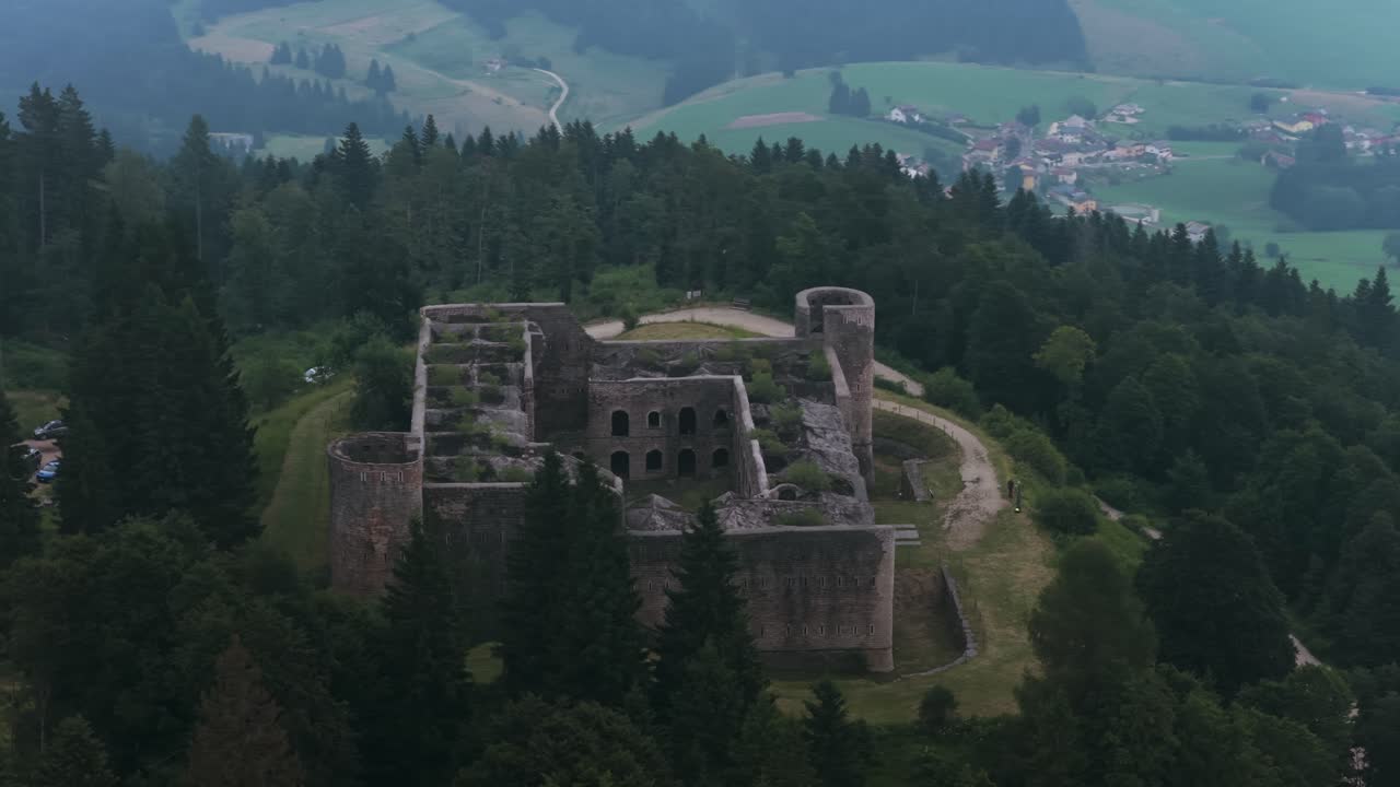 Aerial view of historic Forte Interrotto ruins on hilltop. Overgrown fortress surrounded by pine forest. For travel or history content, Asiago, Italy