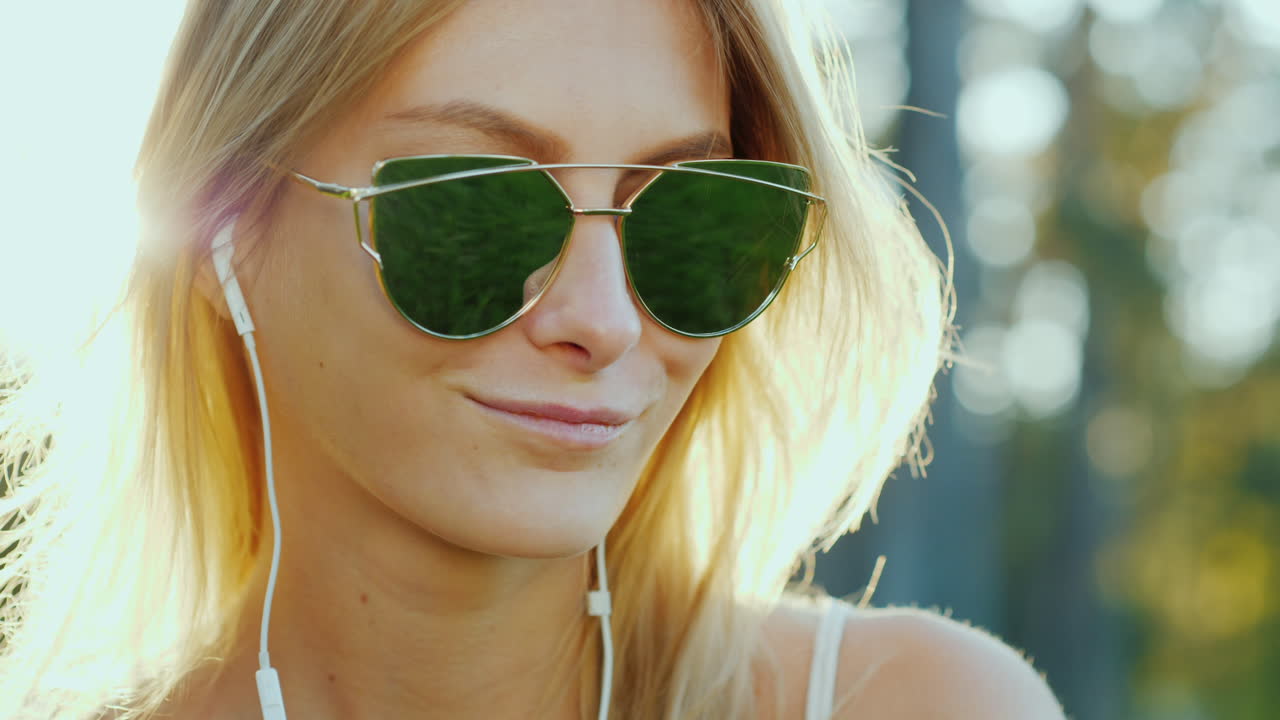 una mujer de aspecto modelo con gafas de sol escucha música al sol de vacaciones los rayos del sol