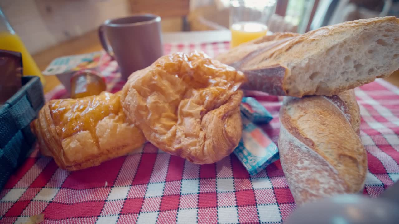 Vista cercana de bollería francesa fresca como cruasanes y pan sobre un mantel de cuadros rojos y blancos durante un desayuno matutino de verano.