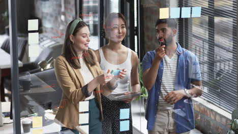 young caucasian woman and asian colleagues brainstorm with sticky notes on a glass wall in a busines