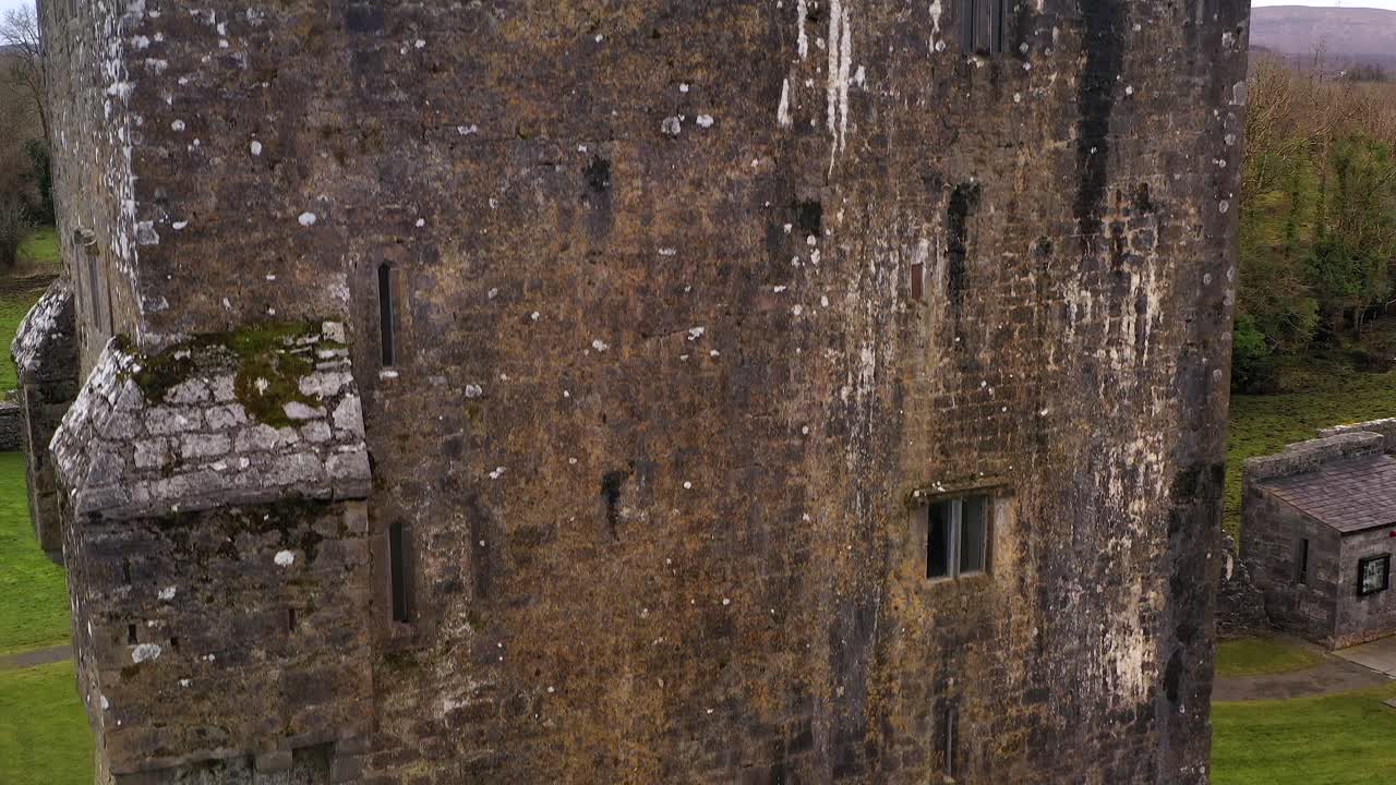 Aerial ascend along weathered wall of Aughnanure Castle, medieval stone structure amid the Irish countryside
