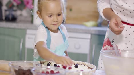 Smiling-little-girl-adding-berries-to-a-pie