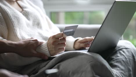 two people sitting together discussing arguing online spending with female hand holding credit card and using laptop for online shopping