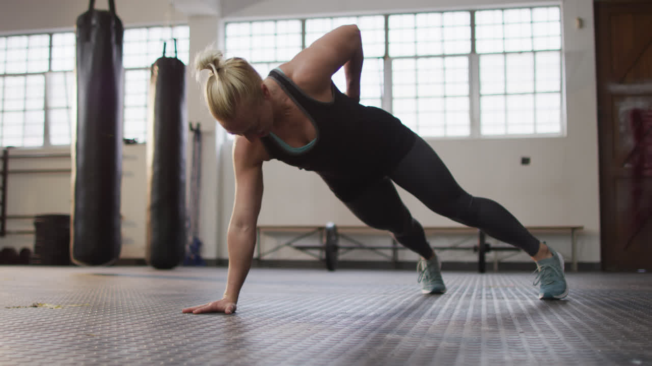 Fit caucasian woman performing one handed push up exercise at the gym