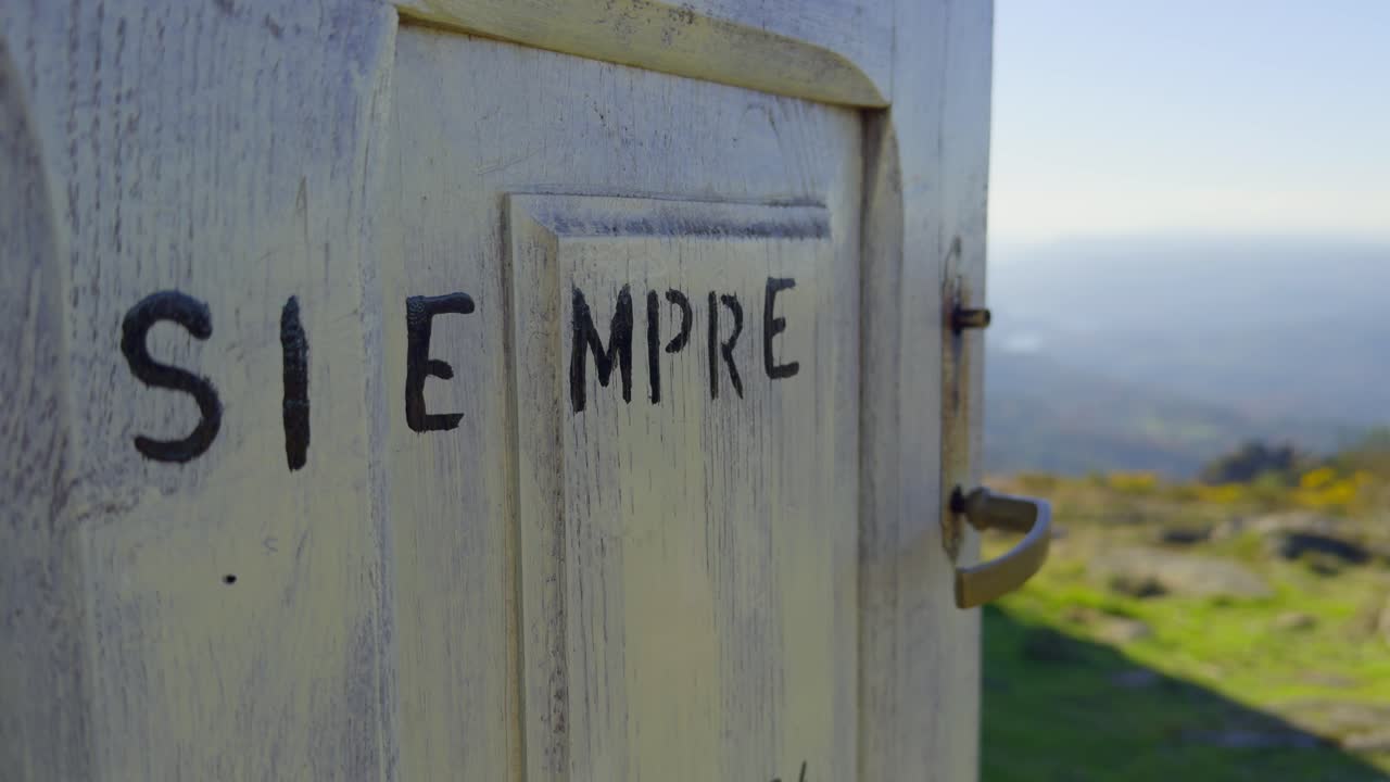 Close Up White Wooden Door With Black Word Written At The Top Of A Mountain