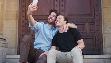 pareja gay tomando selfies en el teléfono móvil sentados al aire libre en las escaleras del edificio