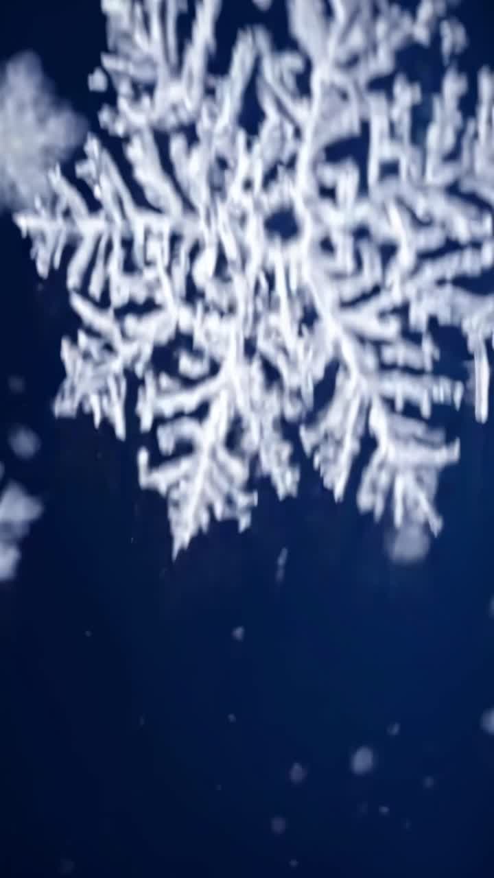 Close-up video of falling snowflakes against a dark blue background, captured from a low angle