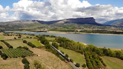 aerial: old diesel train traveling by a lake