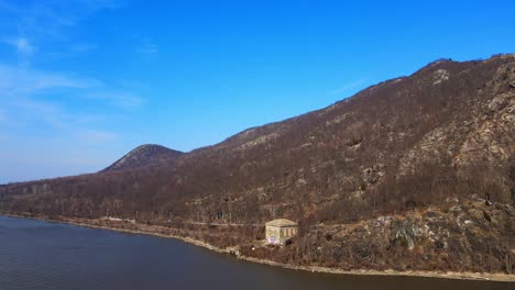 aerial drone footage pulling away from a mountain and over a river in new york state in the hudson valley over the hudson river in early spring by breakneck ridge