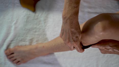 Closeup-overhead-view-of-woman-using-a-gua-sha-tool-to-rub-the-muscles-in-her-calf