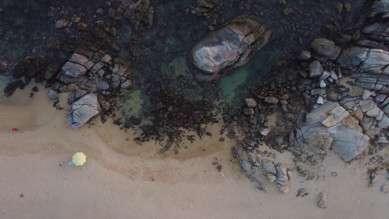 Mesmerizing cenital drone footage circling from the sandy shoreline to the deep turquoise waters, capturing rocks, ocean waves, and the transition from land to sea in a cinematic, smooth movement.