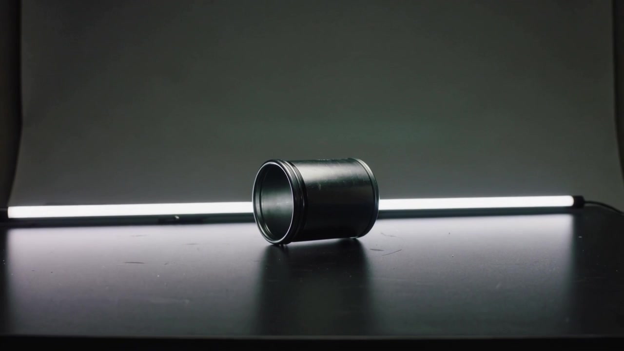 Kameraet trækkes tilbage og afslører en sort metalcylinder på et sort bord, der viser mere af røret og baggrunden.