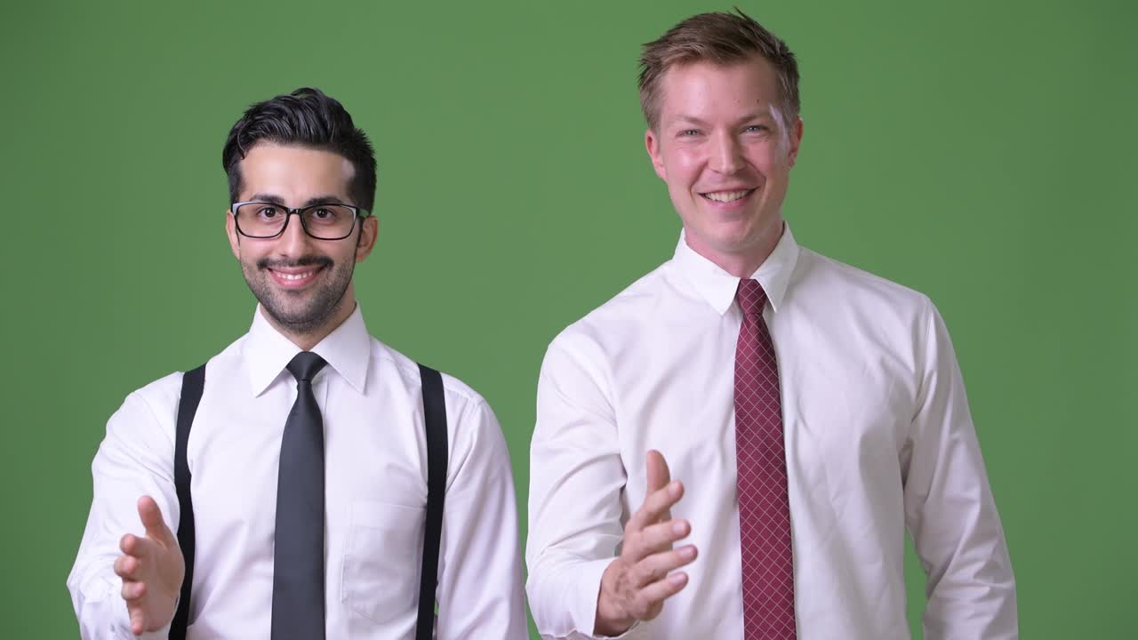 Two young multi-ethnic businessmen working together against green background