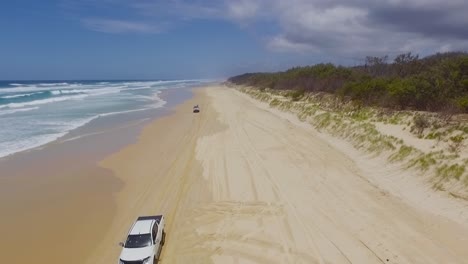 low aerial drone shot looking south down north stradbroke island's main beach as 4x4 four wheel drive trucks and cars drive beneath our vantage point