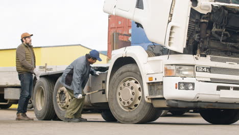 Distant-View-Of-Worker-Fixing-A-Truck-In-A-Logistics-Park-While-Being-Supervised-By-His-Boss