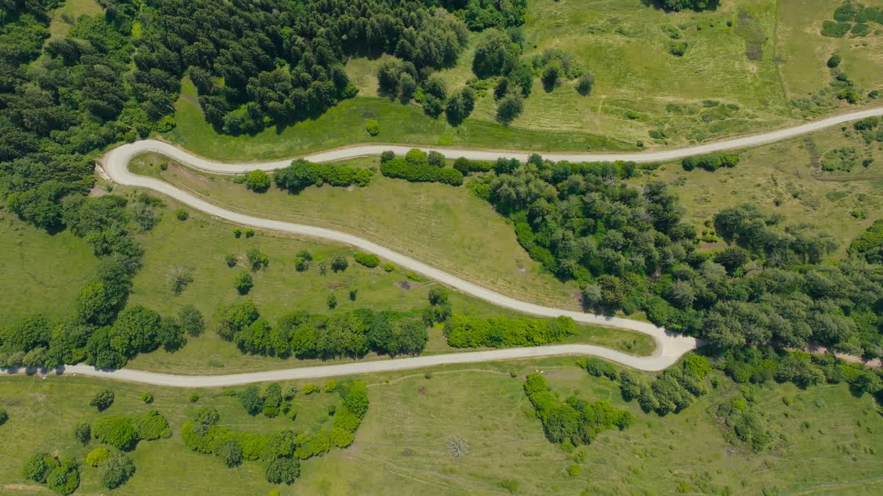 Cinematic top-down drone shot of a curving alpine road weaving through rolling hills and dense greenery in Austria