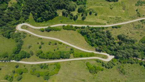 cinematic top-down drone shot of a curving alpine road weaving through rolling hills and dense greenery in austria