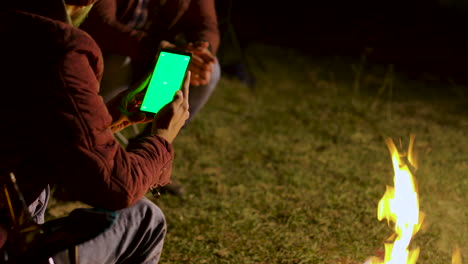 Hombre-Mirando-Este-Teléfono-Con-Pantalla-Verde-Alrededor-De-Una-Fogata