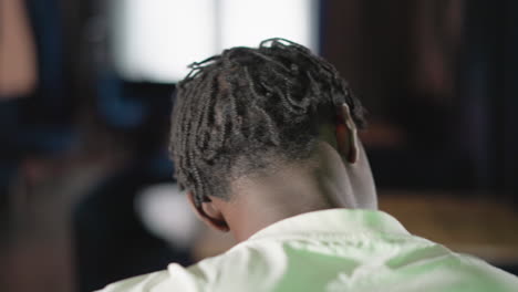 close-up of a person from behind, showing dreadlocks and white shirt. background is blurred, with soft light and warm tones. focus on the back of the head and shoulders in a calm setting