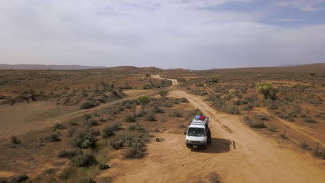 drone orbit around white campervan to reveal australian outback hills