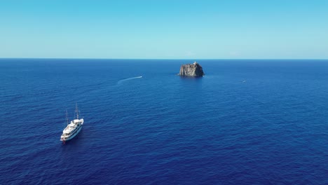 Boats-near-Strombolicchio-Volcano-Island-at-Stromboli,-Aeolian-Islands,-Sicily,-Italy---Aerial-4k