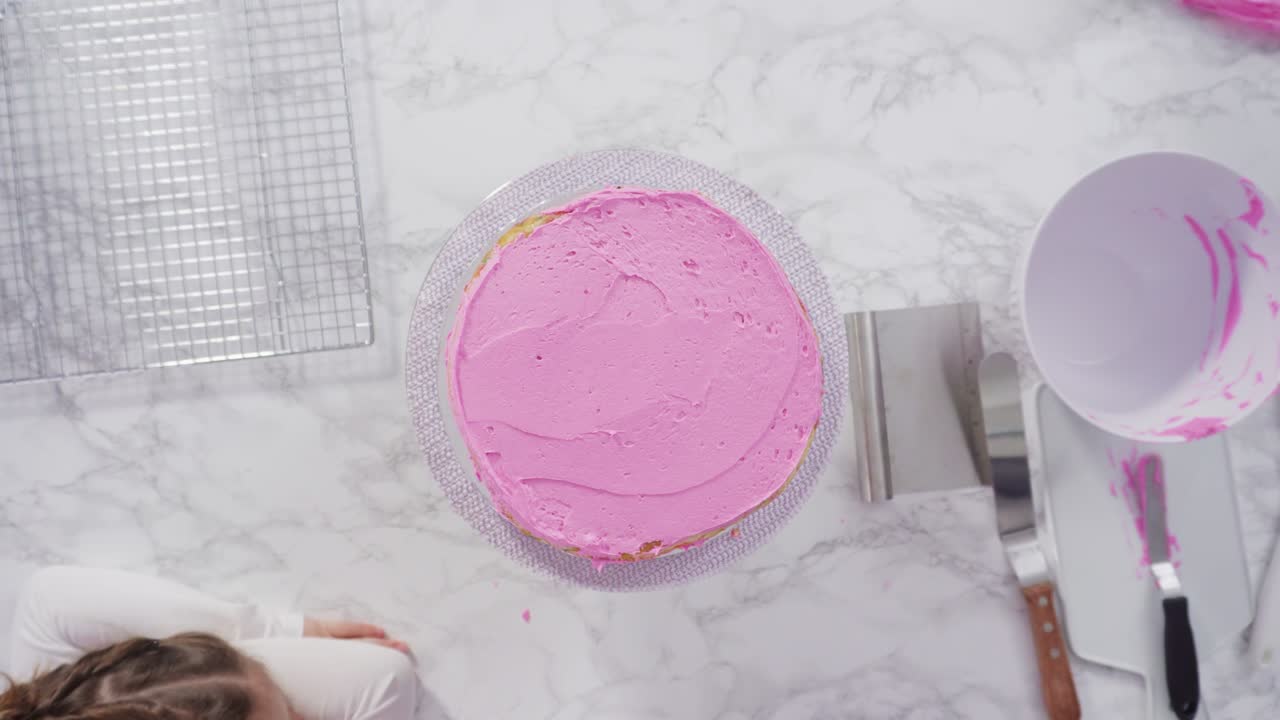 Frosting round funfetti cake layers with pink buttercream frosting.