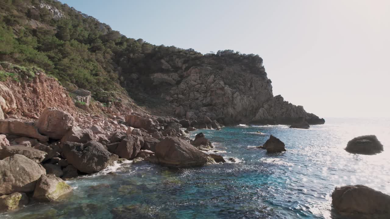 Imagem de drone da costa de Ibiza com falésias rochosas e água azul cristalina do oceano.