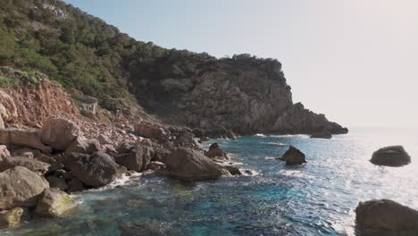 Drone-shot-coast-of-Ibiza-with-rocky-cliffs-and-clear-blue-ocean-water