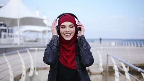 modern muslim girl with hijab covering her head puts headphones on and starts walking somewhere enjoying and dancing to the music