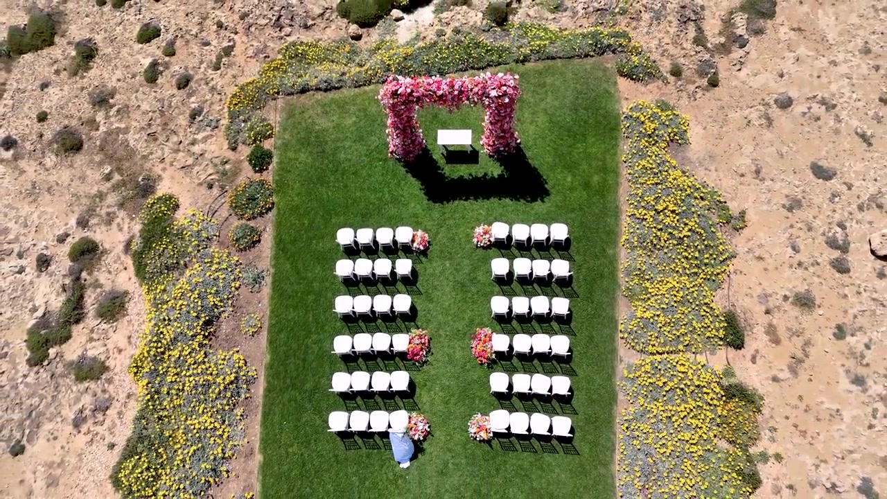Sedie bianche sono disposte in file sull'erba verde per un evento nuziale. Fiori sono posizionati vicino al corridoio. L'allestimento mostra una deliziosa location in giardino pronta per la cerimonia