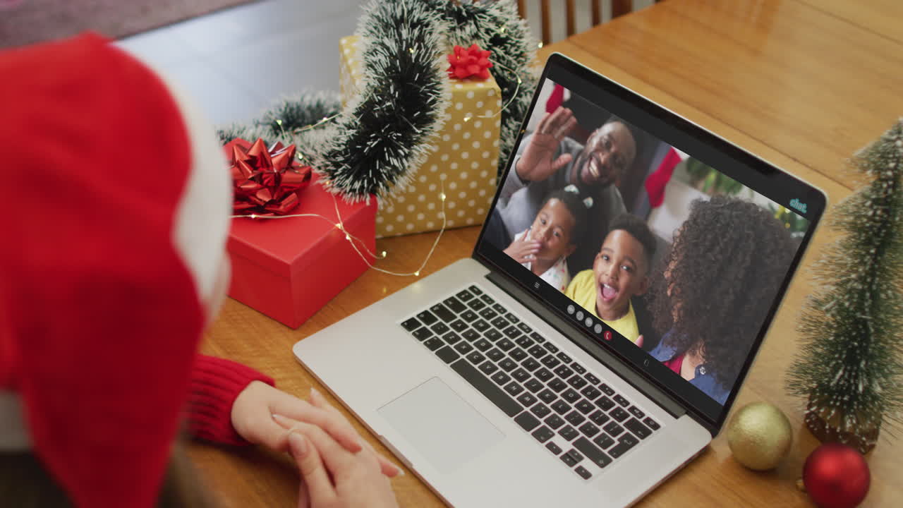 mujer caucásica haciendo una videollamada de navidad en una computadora portátil con una familia afroamericana en la pantalla