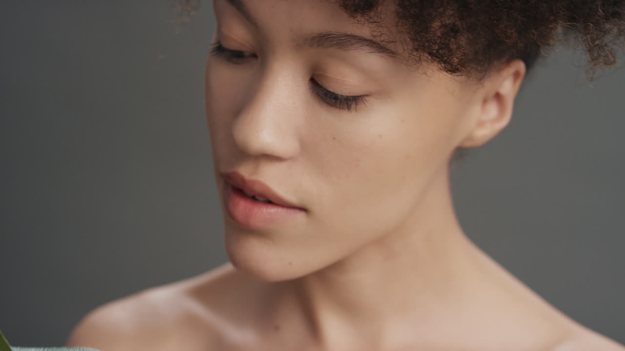retrato de cerca mujer joven atractiva tocando una hoja acariciando piel suave y saludable disfrutando de la belleza natural juguetona sobre un fondo gris concepto de cuidado de la piel