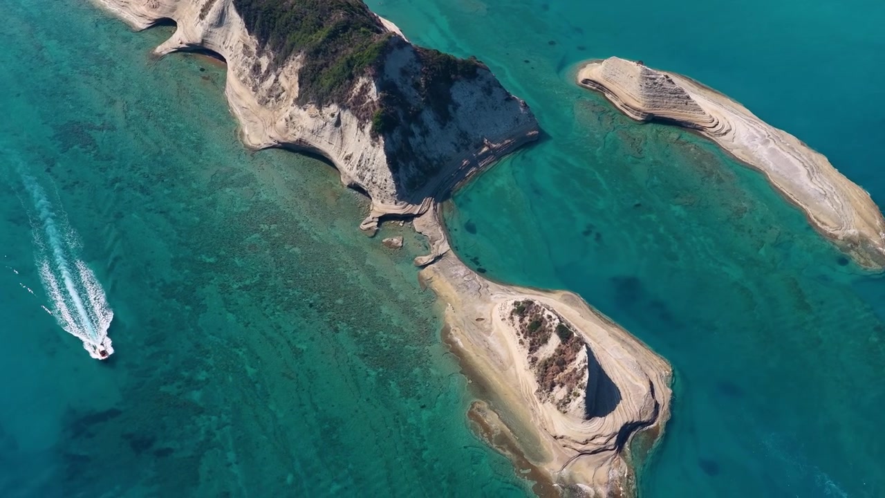 Vista aerea di una barca che si muove attraverso il mare turchese vicino alle spettacolari formazioni rocciose di Capo Drastis a Corfù, Grecia. Paesaggio costiero estivo dall'alto