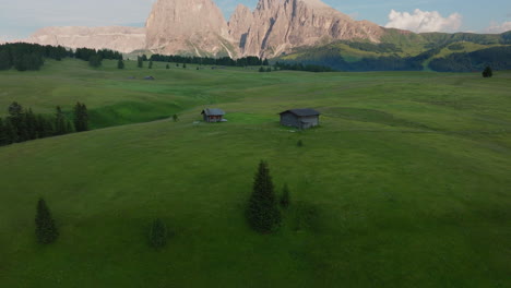 aerial establishing of alpe di siusi grasslands and huts below mountains in sunset light