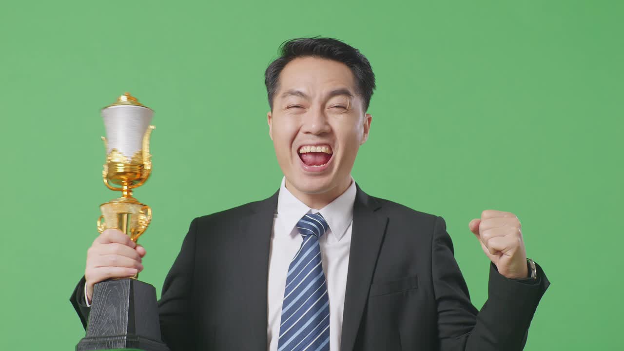 슈트와 타이를 입은 아시아 사업가, 금메달과 트로피를 들고, 첫 번째 우승자로 우승을 축하하는 골을 비명을 지르고 있습니다.