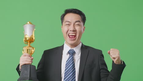 close up of asian business man in a suit and tie with a gold medal and trophy screaming goal celebrating winning as the first winner on green screen background in the studio