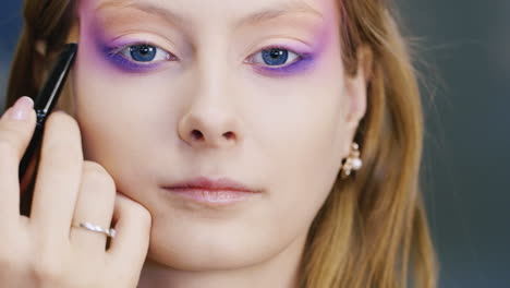 una joven mujer de ojos azules se maquilla en la cara