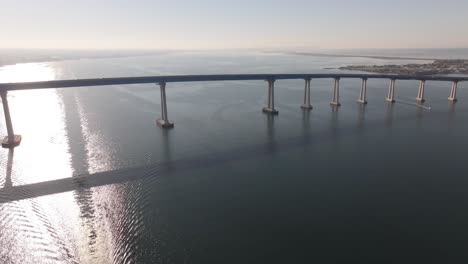 Coronado-Bridge-über-Der-Bucht-Von-San-Diego,-Während-Sich-Das-Sonnenlicht-Im-Wasser-Spiegelt,-Weite-Luftaufnahme