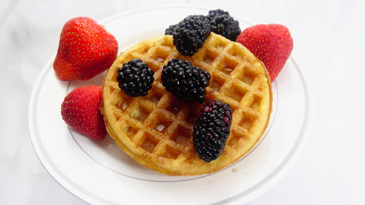 A vibrant breakfast scene featuring fresh strawberries and blackberries paired with warm golden waffles