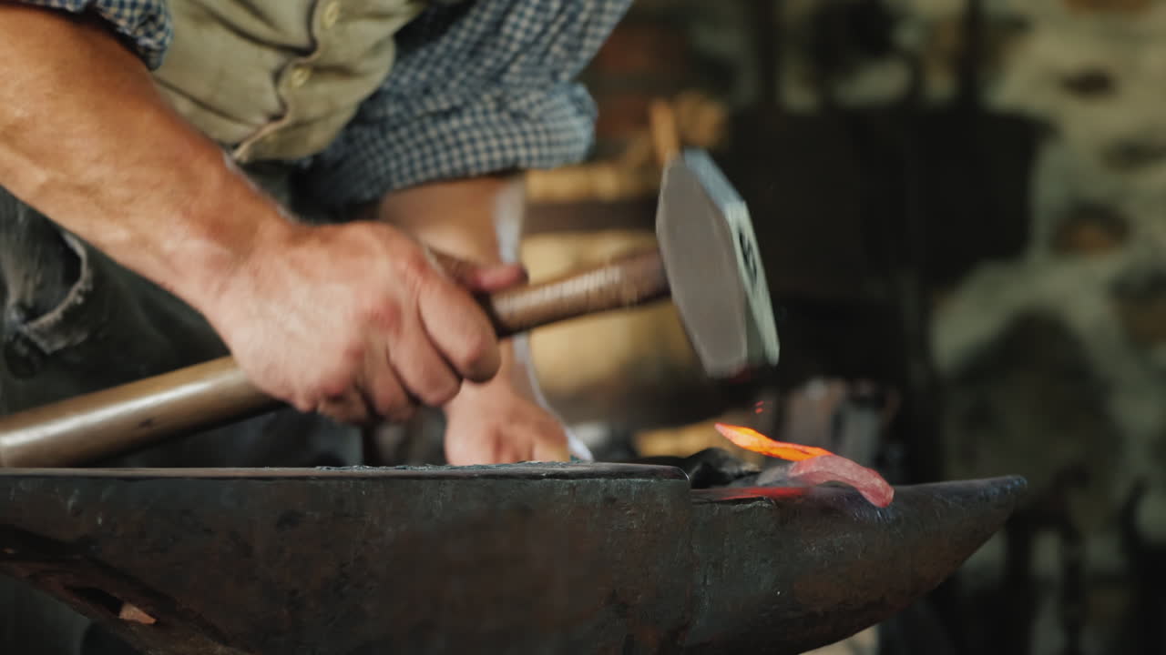 la mano de un herrero con un martillo hace un producto forjado golpeando el yunque