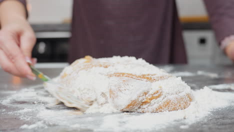 close-up of baker in maroon cloth mixing soft dough with flour on countertop, hands kneading, folding, and blending ingredients for baking