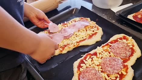 niño poniendo jamón y salami en la masa de pizza