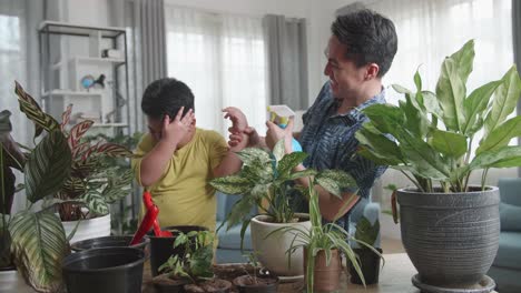 Happy Father And Son Taking Care Of Home Plants At Table Indoors