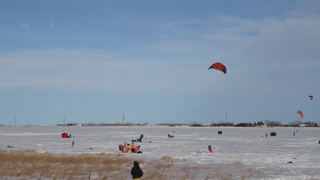 snowkiter readies equipment and waits for the inevitable gust of wind to start kite skiing across a frozen reservoir during a chinook winter’s day in southern alberta