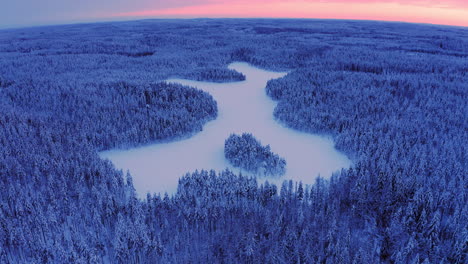 drone shot of snow covered forest and an icy lake with curved horizon by golden hour after sunset