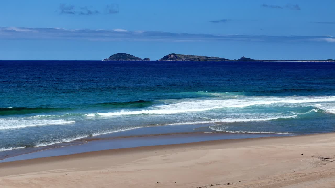 una playa con una orilla de arena y una playa de arena junto a ella y un océano azul con olas blancas vista de pájaro