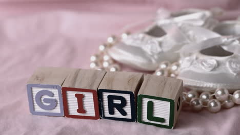 girl in letter blocks beside booties and pearls on pink blanket