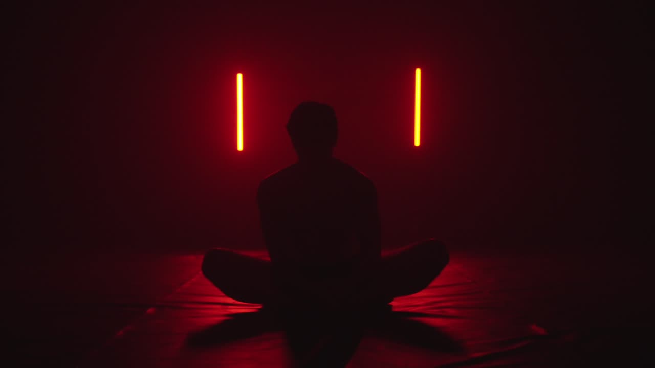 silhouette di una persona che si allunga mentre è seduta in posizione di loto in una stanza rosso scuro